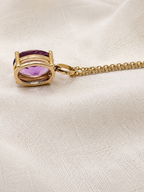 A solid 10k yellow gold pendant necklace featuring the backside of an oval natural purple amethyst gemstone by Ophelisse, resting on a textured beige linen fabric background.