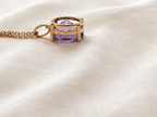 A solid 10k yellow gold pendant necklace with a faceted natural purple amethyst gemstone by Ophelisse, resting on a textured cream-colored fabric background.