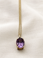 A solid 10k yellow gold chain necklace with an oval natural purple amethyst gemstone pendant by Ophelisse, displayed on a textured off-white fabric background.