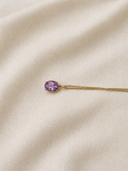 A solid 10k yellow gold chain necklace with an oval natural purple amethyst gemstone pendant by Ophelisse, displayed on a textured cream-colored fabric background.
