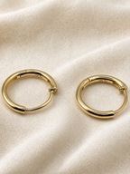 Solid 10k yellow gold huggie hoop earrings displayed on a textured cream fabric background with Ophilesse trademark and gold stamp.