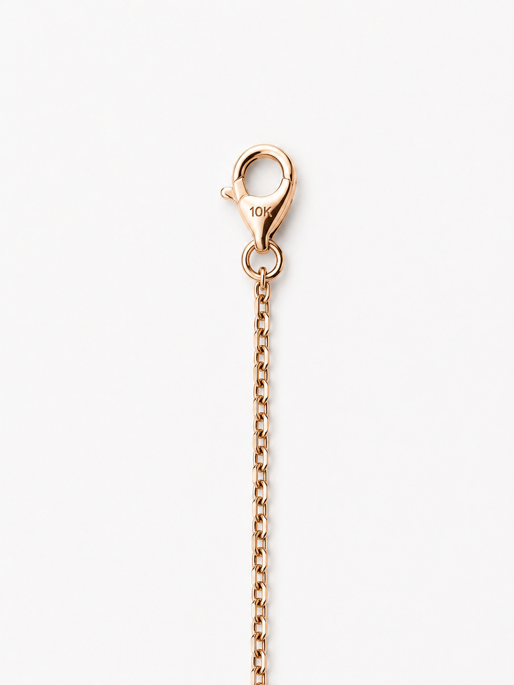 A close-up of a rose gold lobster clasp and extension chain, showing a 10K hallmark on the clasp, set against a plain white background.