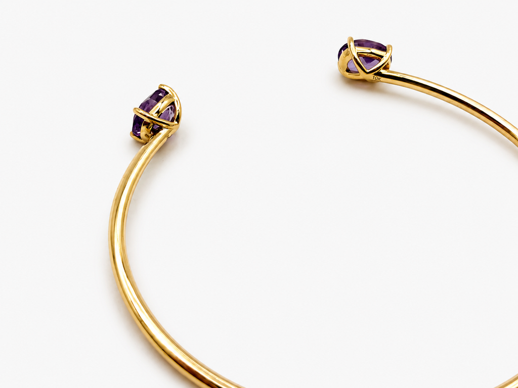 A solid 10k yellow gold bangle with natural amethyst gemstone, oval shape, showing the 10k gold stamp by Ophelisse, photographed on a clean white background, laying flat, angled view, showing the bottom of the stone and the 10k mark.