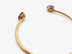 A solid 10k yellow gold bangle with natural amethyst gemstone, oval shape, showing the 10k gold stamp by Ophelisse, photographed on a clean white background, laying flat, angled view, showing the bottom of the stone and the 10k mark.
