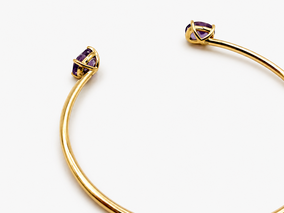 A solid 10k yellow gold bangle with natural amethyst gemstone, oval shape, showing the 10k gold stamp by Ophelisse, photographed on a clean white background, laying flat, angled view, showing the bottom of the stone and the 10k mark.