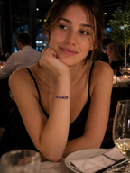 A woman wearing Ophelisse's bracelet on her wrist in a restaurant, the bracelet consists of solid 10k yellow gold with two large oval and two small heart natural purple amethyst gemstones.
