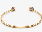 A solid 10k yellow gold open cuff bangle bracelet with two oval amethyst gemstone accents at the ends by Ophelisse, shown on a clean white background, laying flat showing the bottom of the natural amethyst stones, 10k mark, and Ophelisse stamp