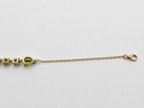 A close-up of a gold chain bracelet showing the bottom view of a pear-shaped and round-shaped natural green peridot gemstone, and solid 10k gold links and 10k hallmark on a plain light gray background.