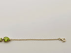 Picture displays part of Ophelisse's solid 10k gold chain bracelet with a pear-shaped natural green peridot gemstone and a smaller green stone, showing Ophelisse's trademark, shown against a plain light background.
