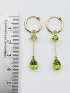 A pair of Ophelisse gold hoop dangle earrings with teardrop  and smaller round natural green peridot gemstones, shown next to a ruler for measurement.