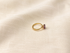 A solid 10k yellow gold ring with a oval natural purple amethyst gemstone by Ophelisse, resting on a textured beige fabric background.
