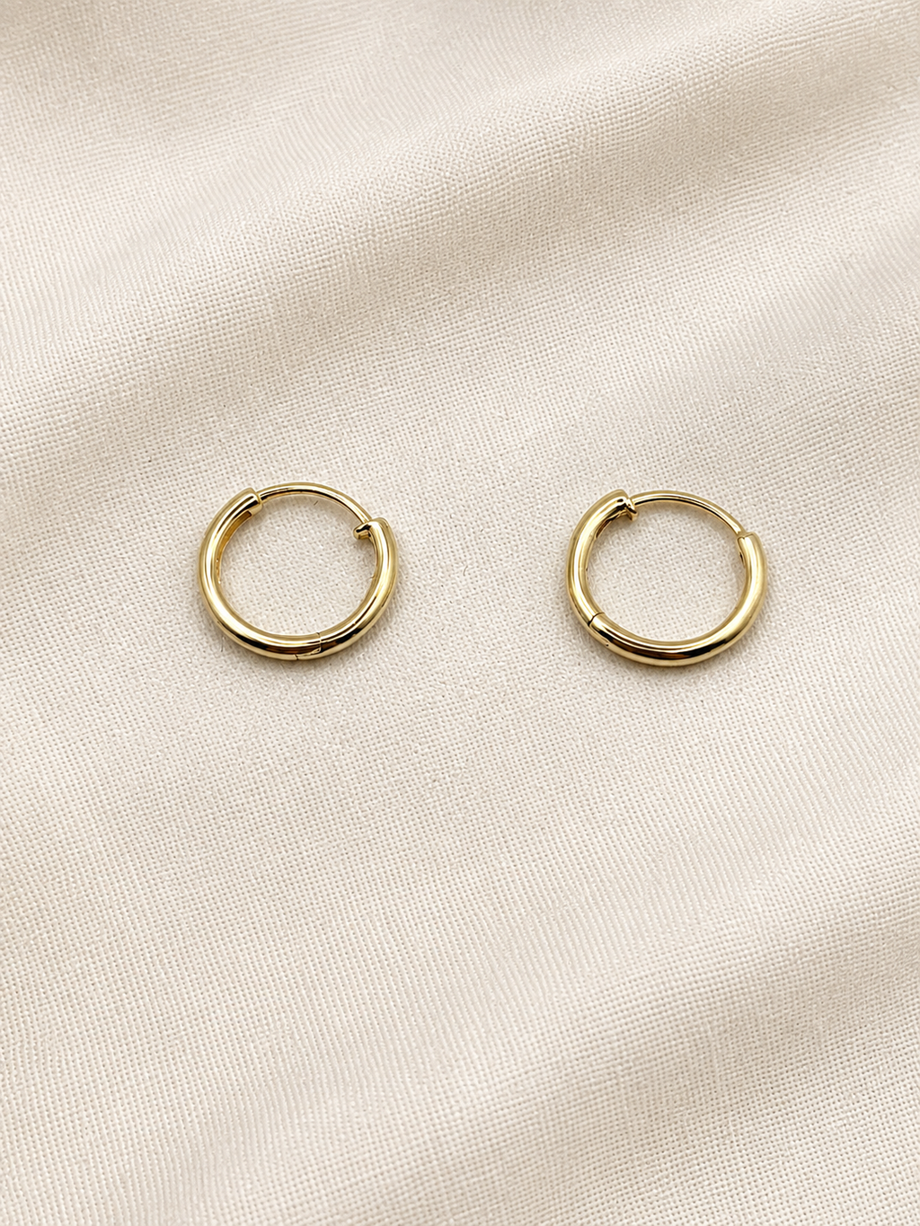 A pair of solid 10k yellow gold dangle earring hoops resting on a textured, light beige fabric background. Trademarked by Ophalisse.