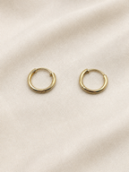 A pair of solid 10k yellow gold dangle earring hoops resting on a textured, light beige fabric background. Trademarked by Ophalisse.