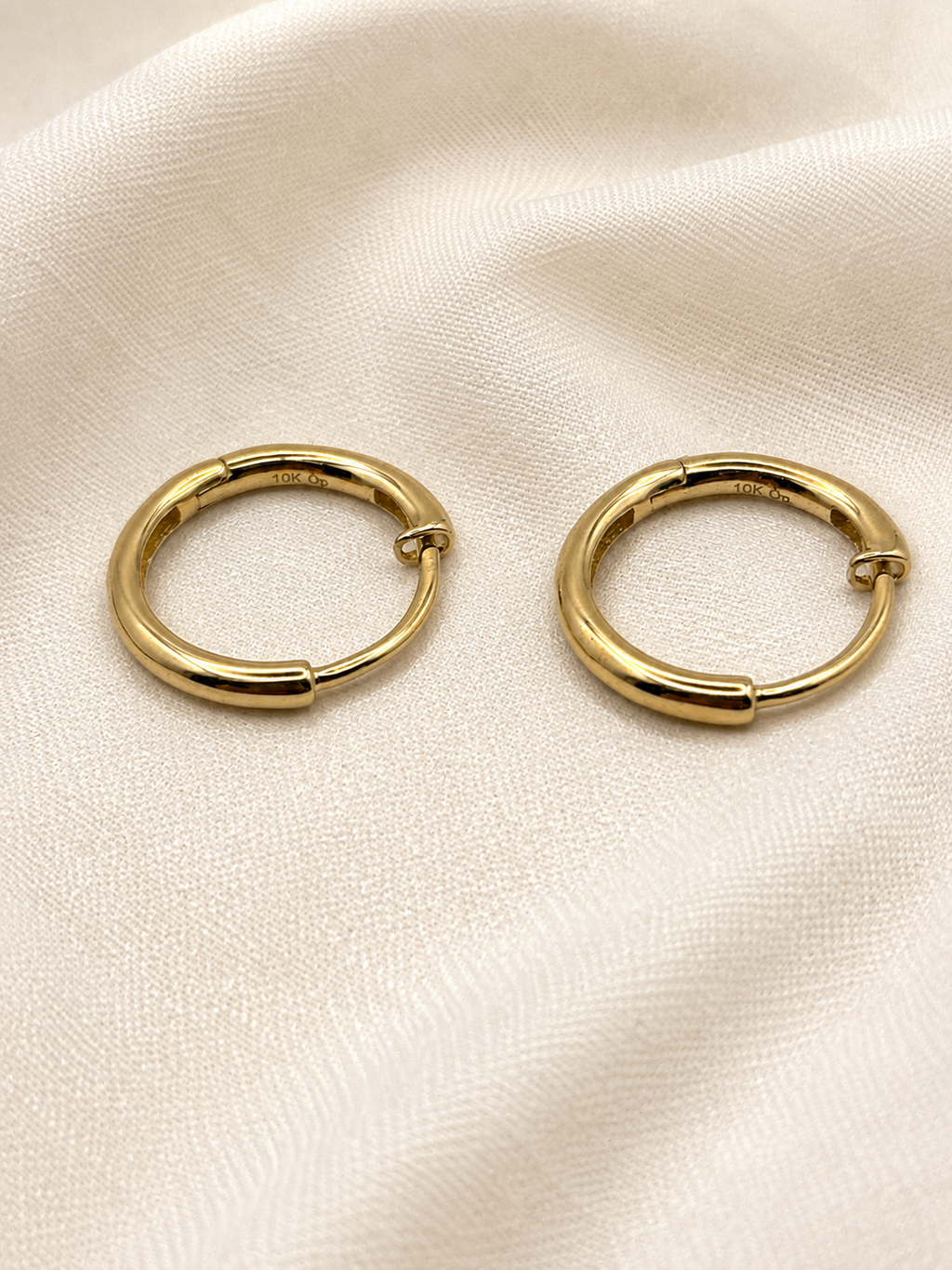 A pair of solid 10k yellow gold dangle earring hoop displayed on a textured, off-white fabric background. Trademarked 10k by Ophelisse.