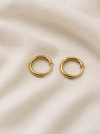 A pair of small solid 10k yellow gold dangle earring hoops resting on a textured, off-white fabric background. Trademarked 10k by Ophelisse.