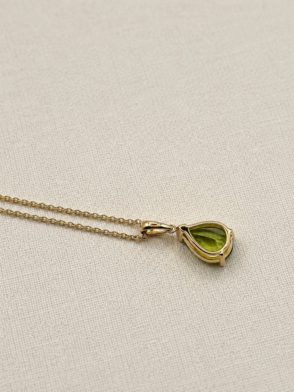A luxurious 10k solid yellow gold chain necklace with a teardrop-shaped natural green peridot gemstone pendant by Ophelisse, back view, displayed on a textured beige fabric background.