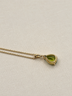 A luxurious 10k solid yellow gold chain necklace with a teardrop-shaped natural green peridot gemstone pendant by Ophelisse, back view, displayed on a textured beige fabric background.