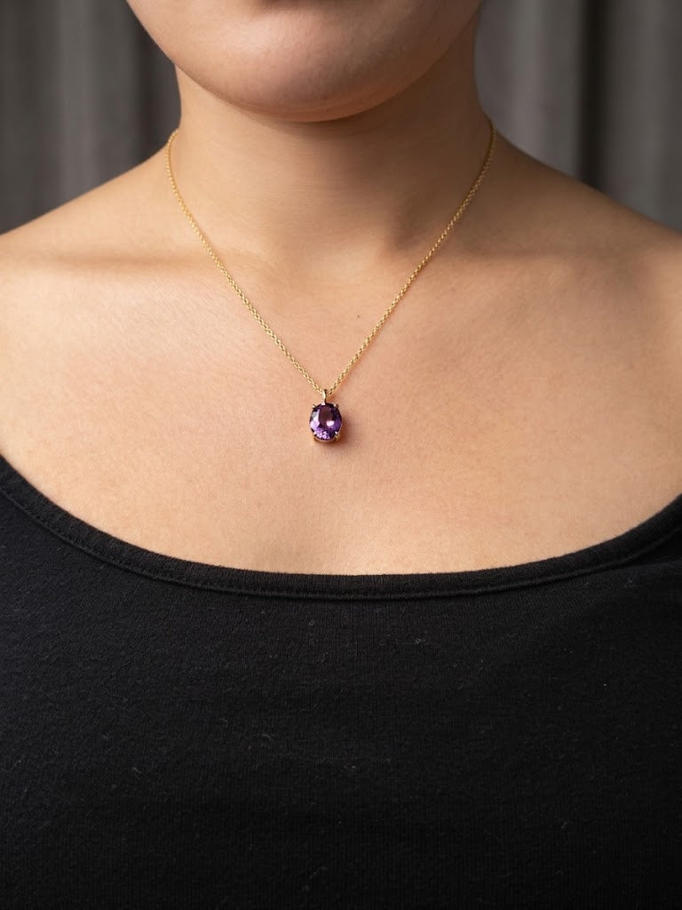 A close-up of a model wearing Ophelisse solid 10k gold chain necklace with an oval purple natural amethyst gemstone pendant at 18 inch in length