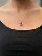 A close-up of a real model wearing Ophelisse solid 10k yellow gold chain necklace with an oval purple natural amethyst gemstone pendant, at 20 inch necklace length.