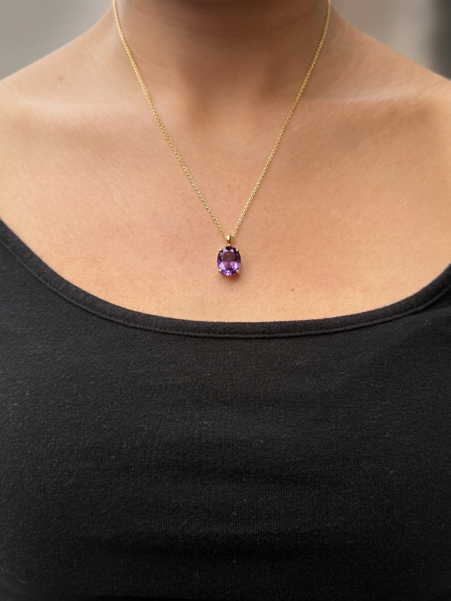 A close-up of a real model wearing Ophelisse solid 10k yellow gold chain necklace with an oval purple natural amethyst gemstone pendant, at 20 inch necklace length.