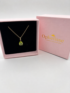 Solid 10k yellow Gold fine jewelry necklace with a tear-shaped green peridot necklace natural gemstone inside of an Ophelisse pink box with golden elegant writing with a fine sun in the background