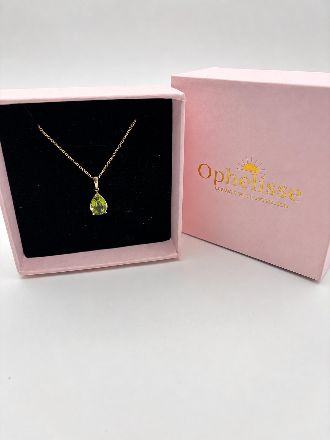 Solid 10k yellow Gold fine jewelry necklace with a tear-shaped green peridot necklace natural gemstone inside of an Ophelisse pink box with golden elegant writing with a fine sun in the background