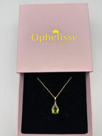 An elegant solid 10k yellow gold chain necklace with a teardrop-shaped green peridot natural gemstone pendant, presented inside an open pink jewelry box with the brand name 'Ophelisse' printed in gold on the lid.