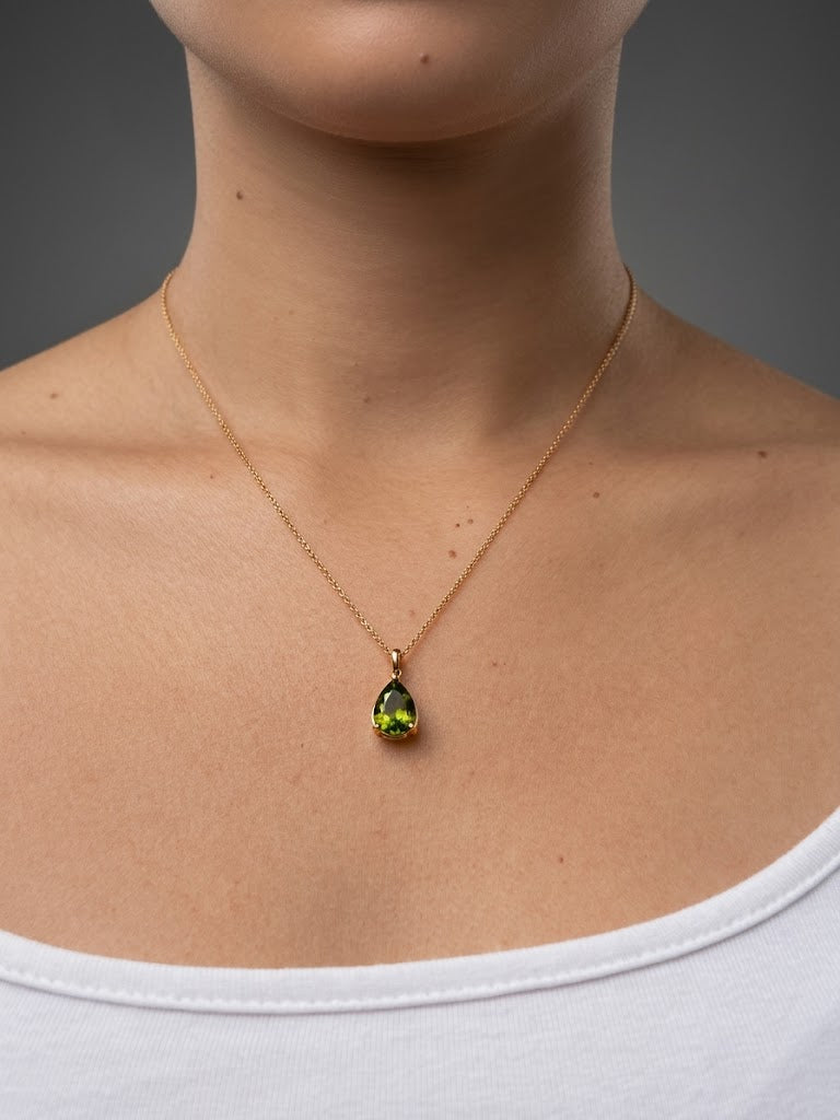 A close-up of a real model wearing Ophelisse solid 10k gold chain necklace with a small pear-shaped green natural peridot gemstone pendant, at 18-inch