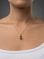 A close-up of a real model wearing Ophelisse solid 10k gold chain necklace with a small pear-shaped green natural peridot gemstone pendant, at 18-inch