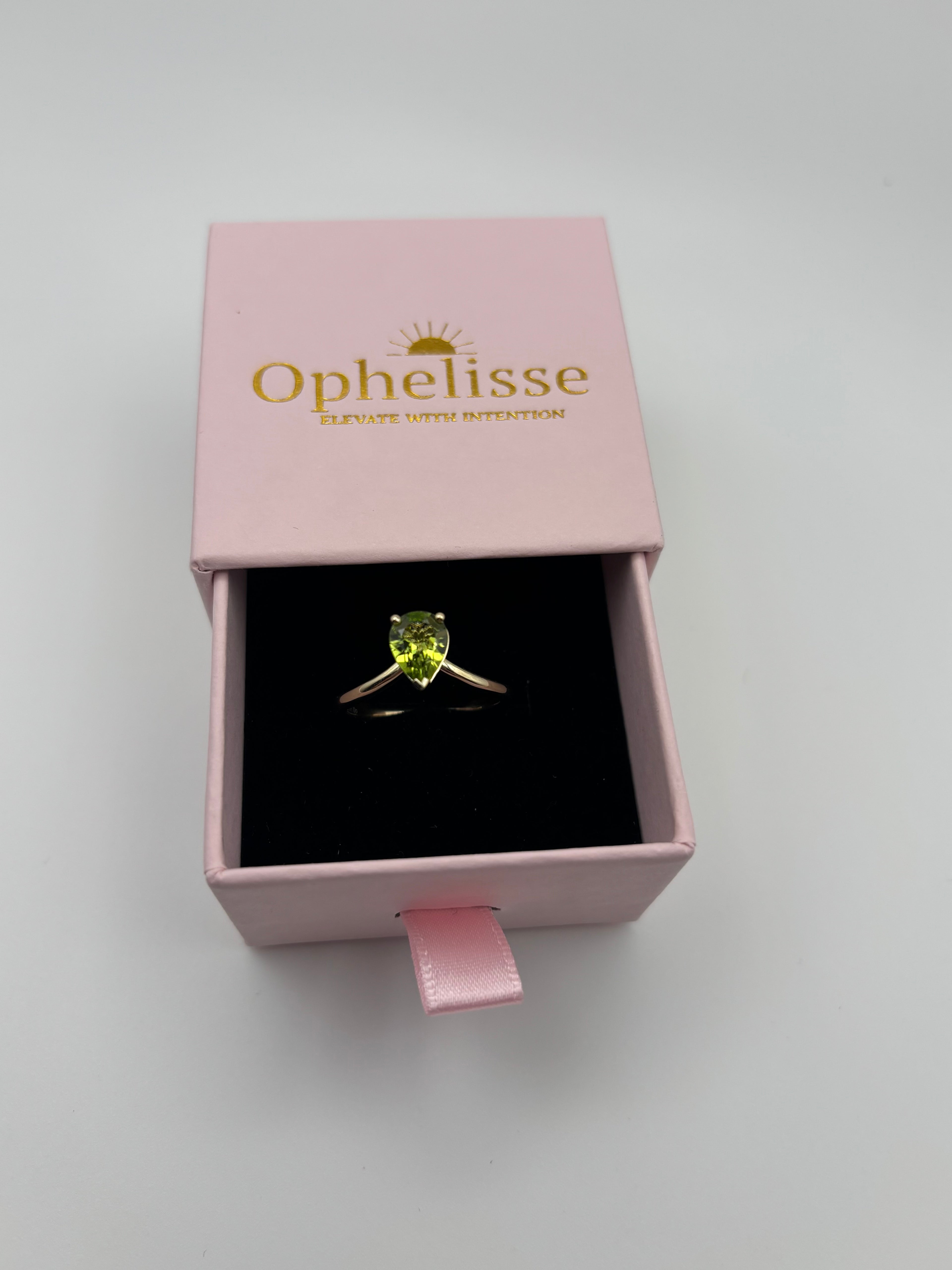 A solid 10k yellow gold ring with a natural green pear-shaped peridot gemstone displayed in a black velvet-lined pink Ophelisse box, a luxurious unwrapping experience.