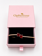 A solid 10k rose gold cuff bracelet with two heart-shaped natural red garnet gemstones, presented inside an open pink Ophelisse gift box with a black interior.
