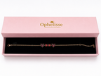 A solid 10k rose gold chain bracelet with two natural red heart-shaped and two round-shaped garnet gemstones, presented in an open pink Ophelisse jewelry box with a black velvet interior.