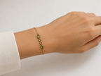 A close up on Ophelisse solid 10k yellow gold chain bracelet with natural green peridot gemstones on a wrist against a neutral background