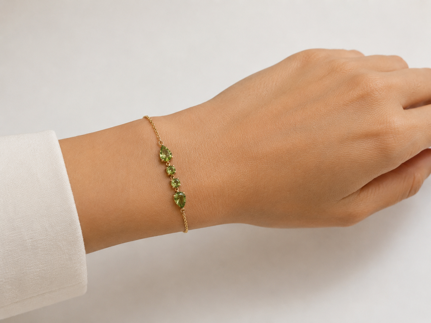 A close up on Ophelisse solid 10k yellow gold chain bracelet with natural green peridot gemstones on a wrist against a neutral background