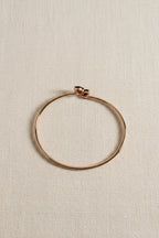Solid 10k rose gold bangle by Ophelisse, featured two natural red garnet gemstones, flat top view on a light beige linen background