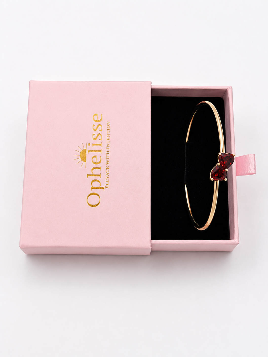 A solid 10k rose gold bangle bracelet with a double heart charm set with deep red natural garnet gemstones, presented in a pink Ophelisse gift box with a black interior, top view