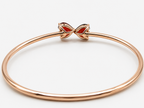 A solid 10k rose gold bangle bracelet with a decorative bow-shaped clasp featuring red natural garnet, positioned flat on a clean white background showing the bottom view of the stones and Ophelisse trademark and 10k mark