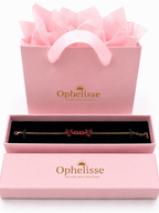 A solid 10k rose gold chain bracelet with natural red garnet gemstones displayed in an open pink Ophelisse presentation box, with a matching pink gift bag filled with tissue paper behind it on a white background.