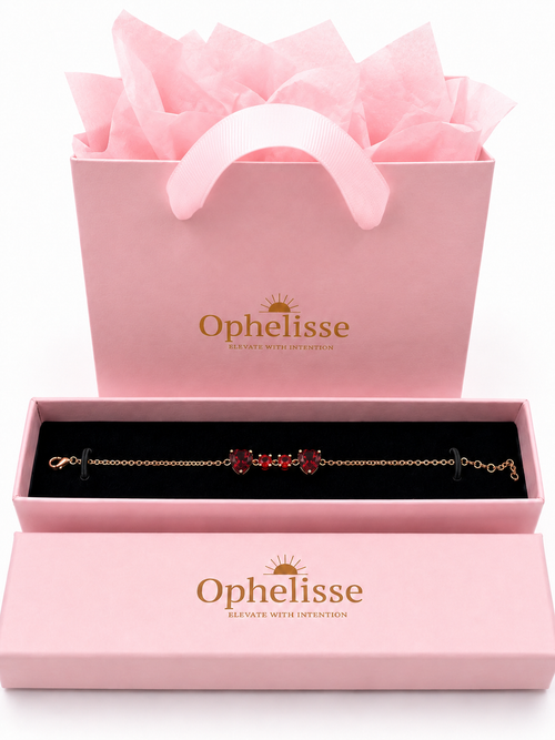A solid 10k rose gold chain bracelet with natural red garnet gemstones displayed in an open pink Ophelisse presentation box, with a matching pink gift bag filled with tissue paper behind it on a white background.