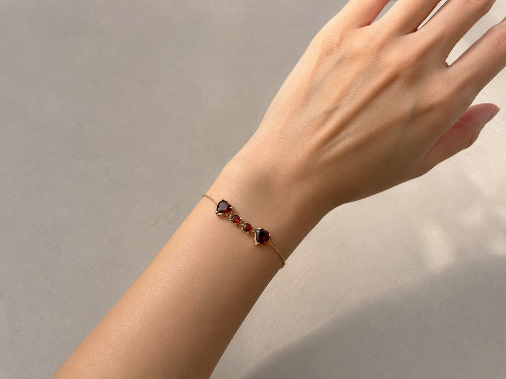 Hand wearing Ophelisse solid 10k rose gold chain bracelet with natural red garnet gemstones in natural light and neutral background