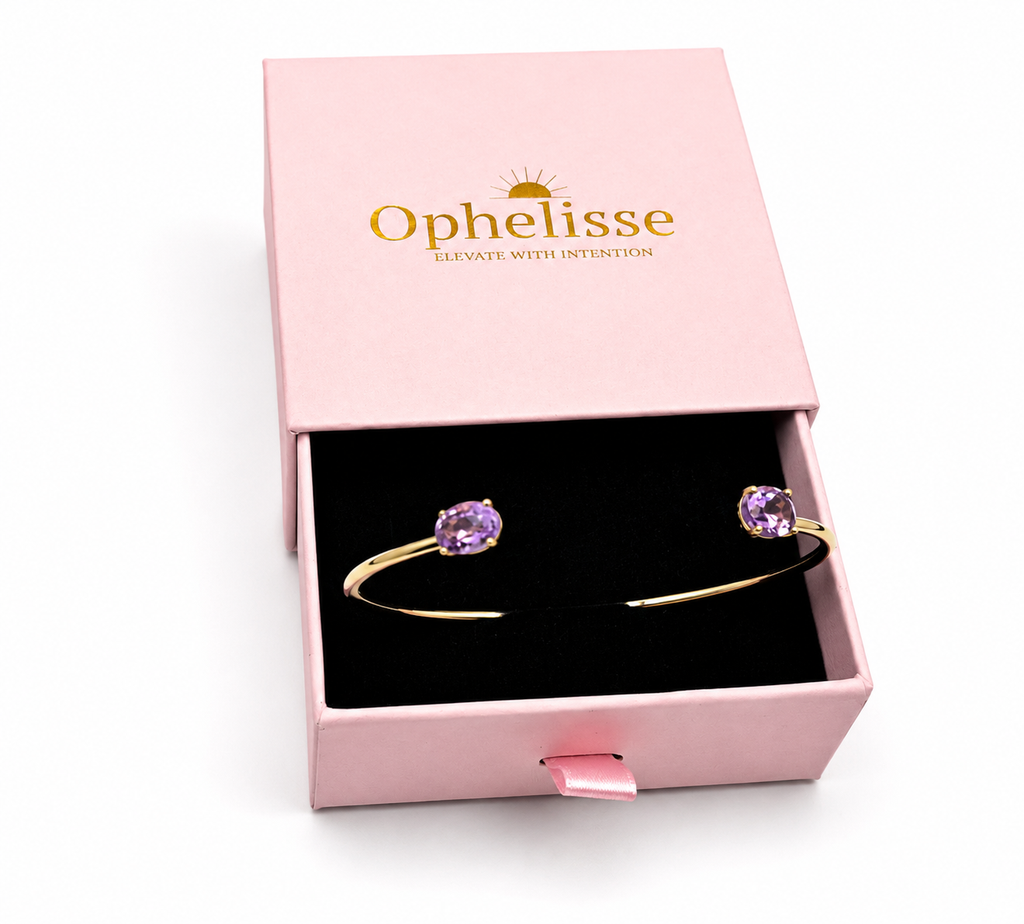 A solid 10k yellow gold bangle with natural oval purple amethyst gemstones, presented in an open pink Ophelisse jewelry box with a black velvet insert.