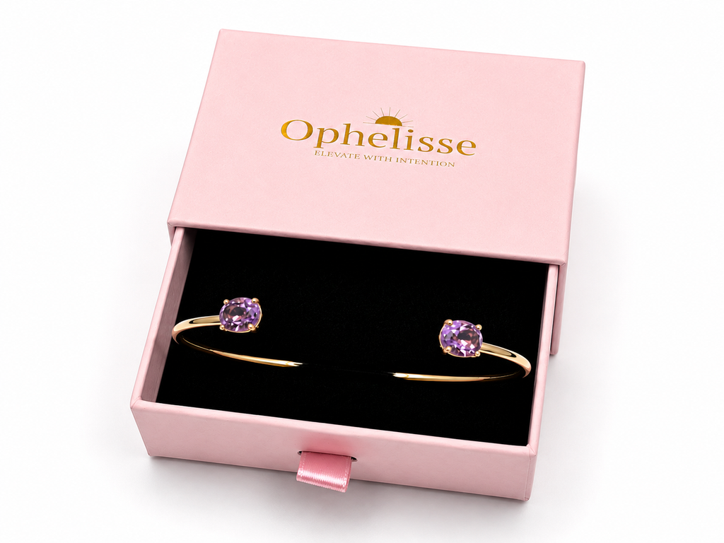 A solid 10k yellow gold bangle with natural oval purple amethyst gemstones, presented in an open pink Ophelisse jewelry box with a black velvet interior.