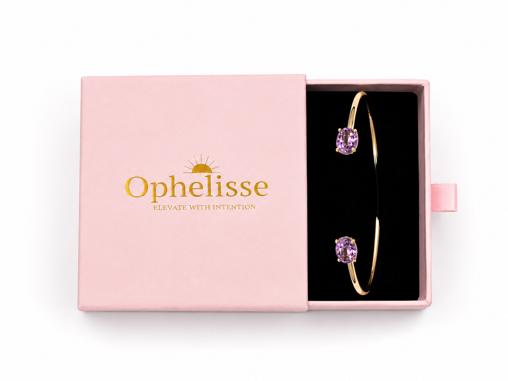 A pink Ophelisse jewelry box shown open, revealing a solid 10k yellow gold bangle bracelet with two natural purple oval amethyst gemstones on a black insert, against a white background.