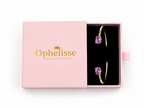 A pink Ophelisse jewelry box shown open, revealing a solid 10k yellow gold bangle bracelet with two natural purple oval amethyst gemstones on a black insert, against a white background.