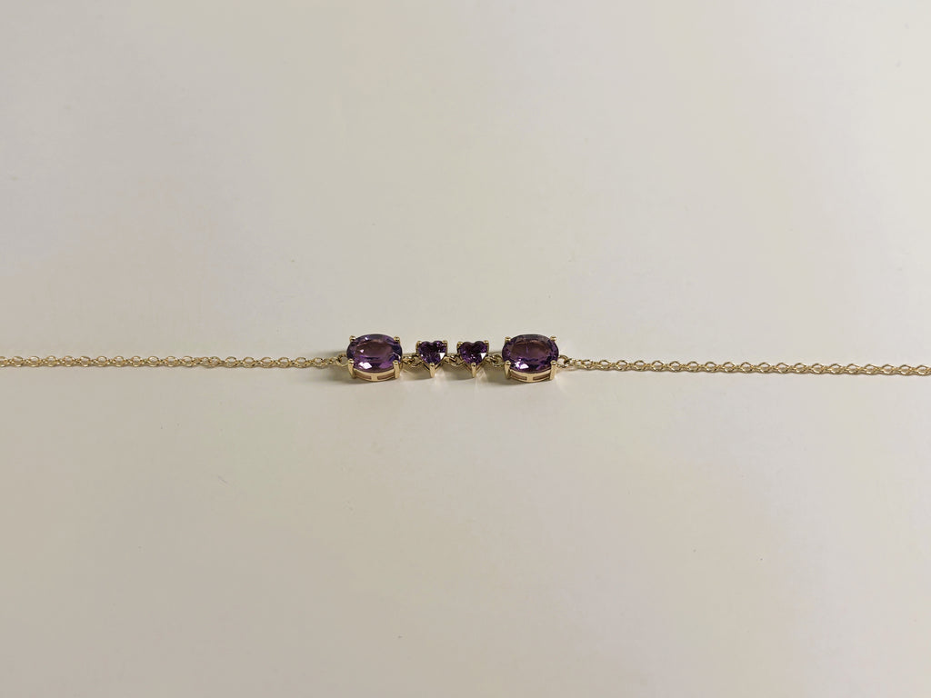 Ophelisse solid 10k yellow gold chain bracelet featuring two oval and two heart natural purple amethyst gemstones, shown closed up and side angle view against a plain off-white background.