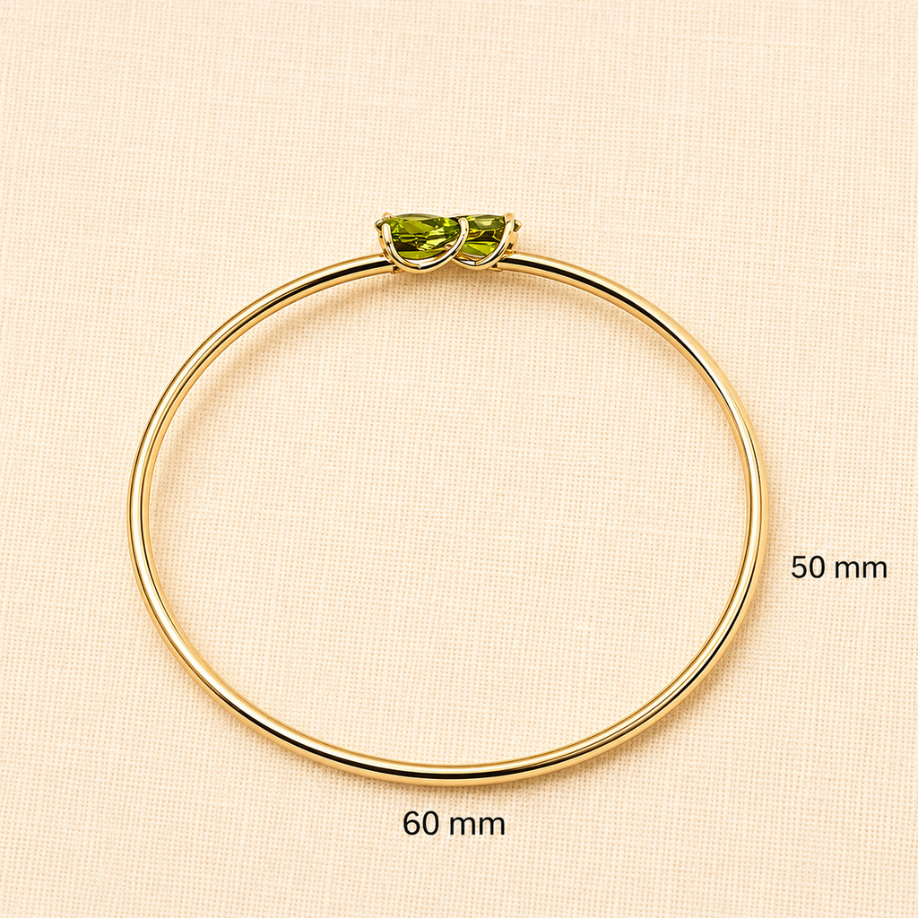 Solid 10k yellow gold bangle bracelet with two natural green peridot gemstone setting by Ophelisse, shown on a light beige textured background with size markings of 50 mm and 60 mm.