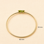 Solid 10k yellow gold bangle bracelet with two natural green peridot gemstone setting by Ophelisse, shown on a light beige textured background with size markings of 50 mm and 60 mm.