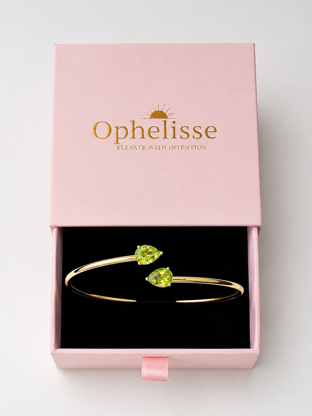 A solid 10k gold bangle bracelet with two natural green teardrop peridot gemstones, presented in an open pink Ophelisse gift box with a black interior, showing the top side angle view.