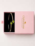Top view of a solid 10k yellow gold bangle bracelet with two natural green pear-shaped peridot gemstones, presented in Ophelisse's pink gift box. 