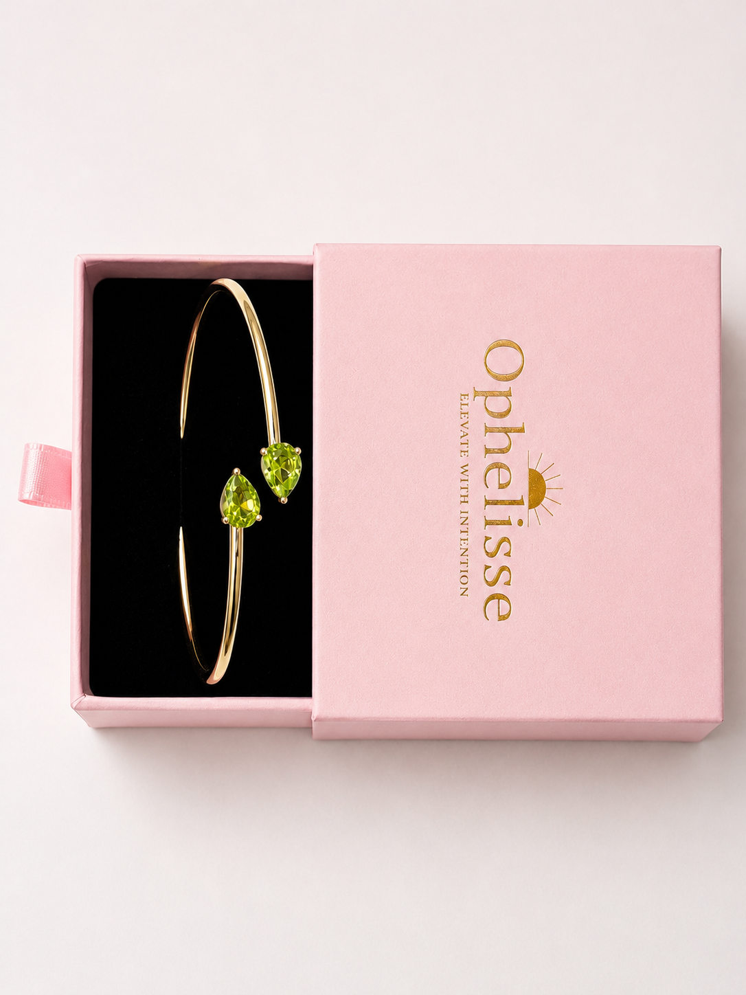Top view of a solid 10k yellow gold bangle bracelet with two natural green pear-shaped peridot gemstones, presented in Ophelisse's pink gift box. 